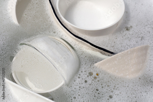 Dishes and bowls in water and bubbles of dishwashing liquid. Kitchen work