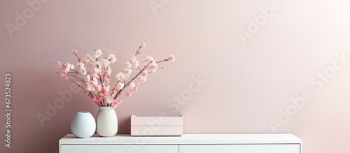 Home decor with a simple arrangement of furniture and decorative items in a living room including a white commode book vase holding dried flowers modern sculpture casket bowl pink wall and  photo
