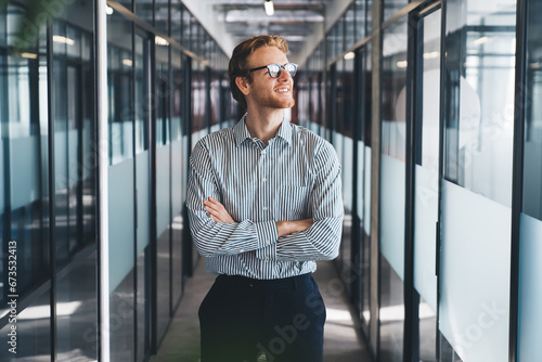 Positive businessman in modern office corridor with arms crossed