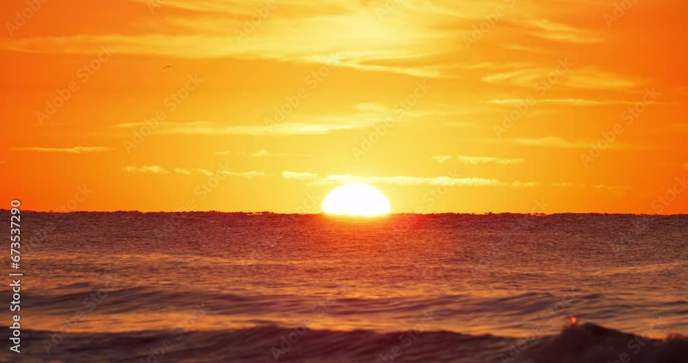 Zoomed in shot of the sun rising over the horizon with beach waves crashing in the foreground and birds flying in the sky. Zoomed in shot of the sun rising over the horizon with beach waves crashing in the foreground and birds flying in the sky.