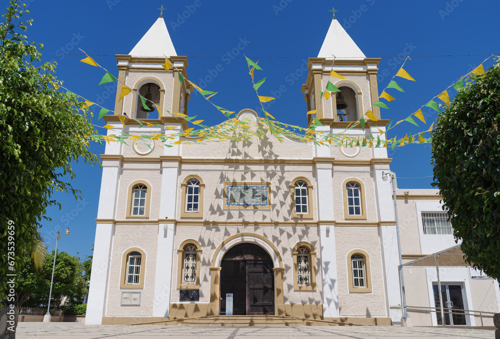 The Mision de San Jose Church in San Jose del Cabo, Mexico. The building is decorated with strings of green and yellow triangular flags against a blue sky.