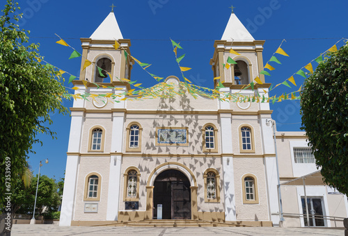 The Mision de San Jose Church in San Jose del Cabo, Mexico. The building is decorated with strings of green and yellow triangular flags against a blue sky.