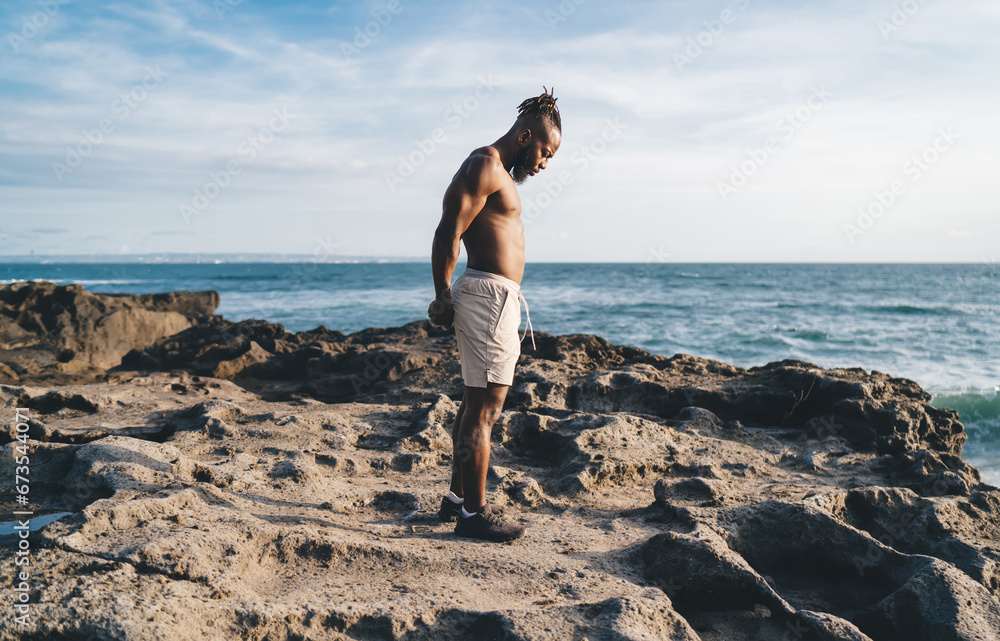 Black man standing and exercising on rocky seashore