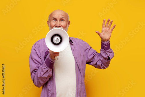 old bald grandfather announces information through megaphone on yellow isolated background, pensioner with loudspeaker