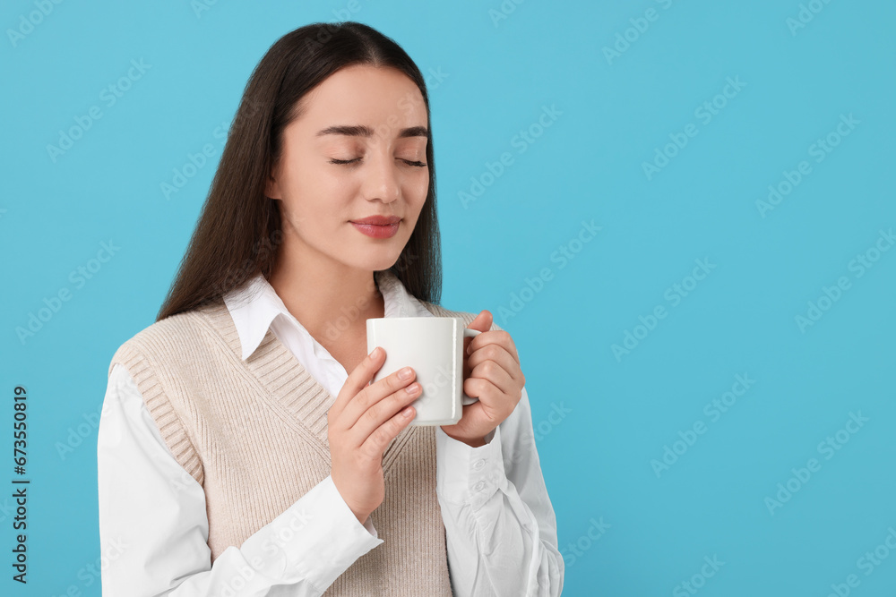 Beautiful young woman holding white ceramic mug on light blue background, space for text Beautiful young woman holding white ceramic mug on light blue background, space for text