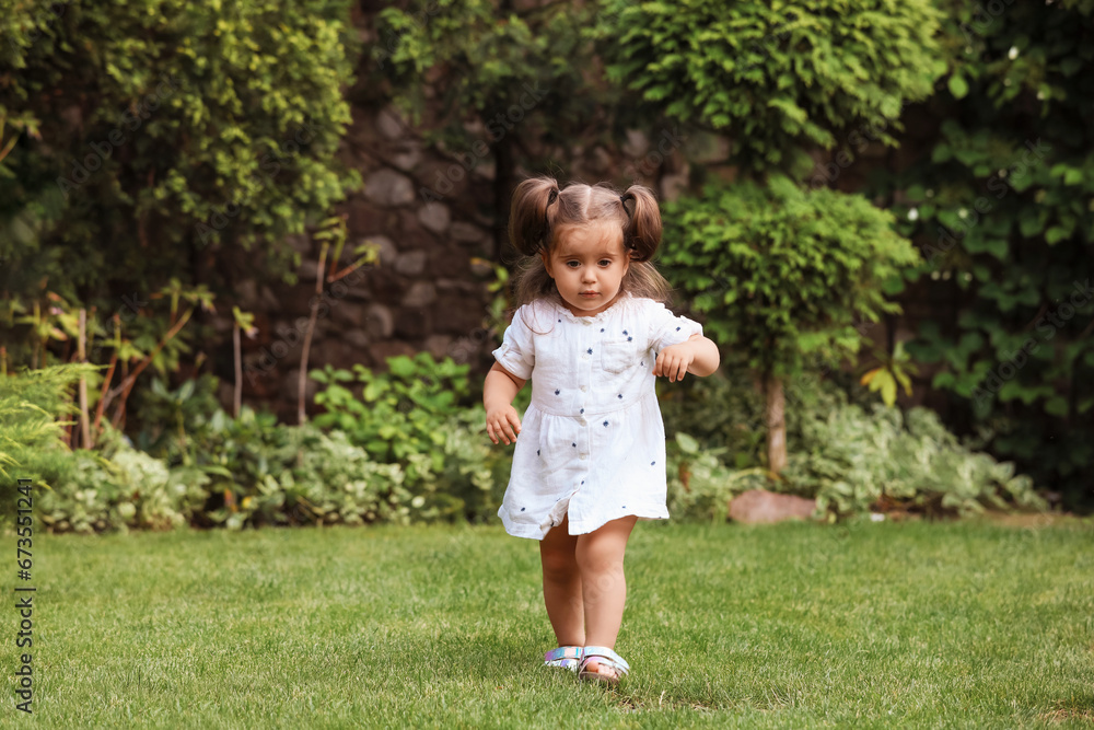 Cute little girl walking on green grass in park Cute little girl walking on green grass in park