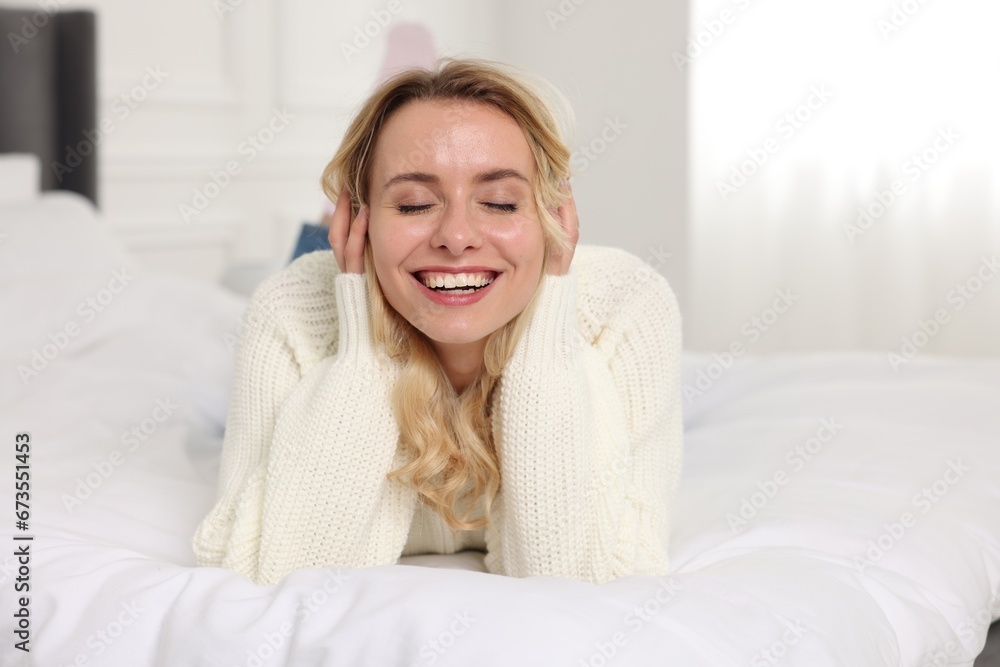 Happy woman in stylish warm sweater lying on bed indoors Happy woman in stylish warm sweater lying on bed indoors