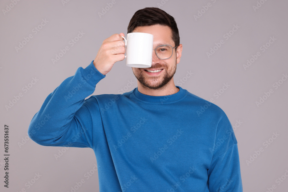 Portrait of happy man covering eye with white mug on grey background Portrait of happy man covering eye with white mug on grey background