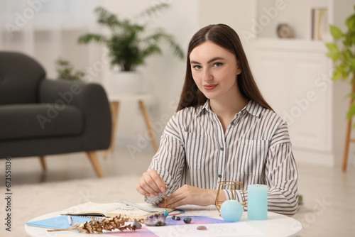 Woman using pendulum for fate forecast at table indoors. Astrological predictions