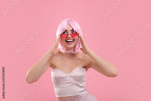 Pink look. Beautiful girl in wig and clothes wearing bright sunglasses on color background © New Africa