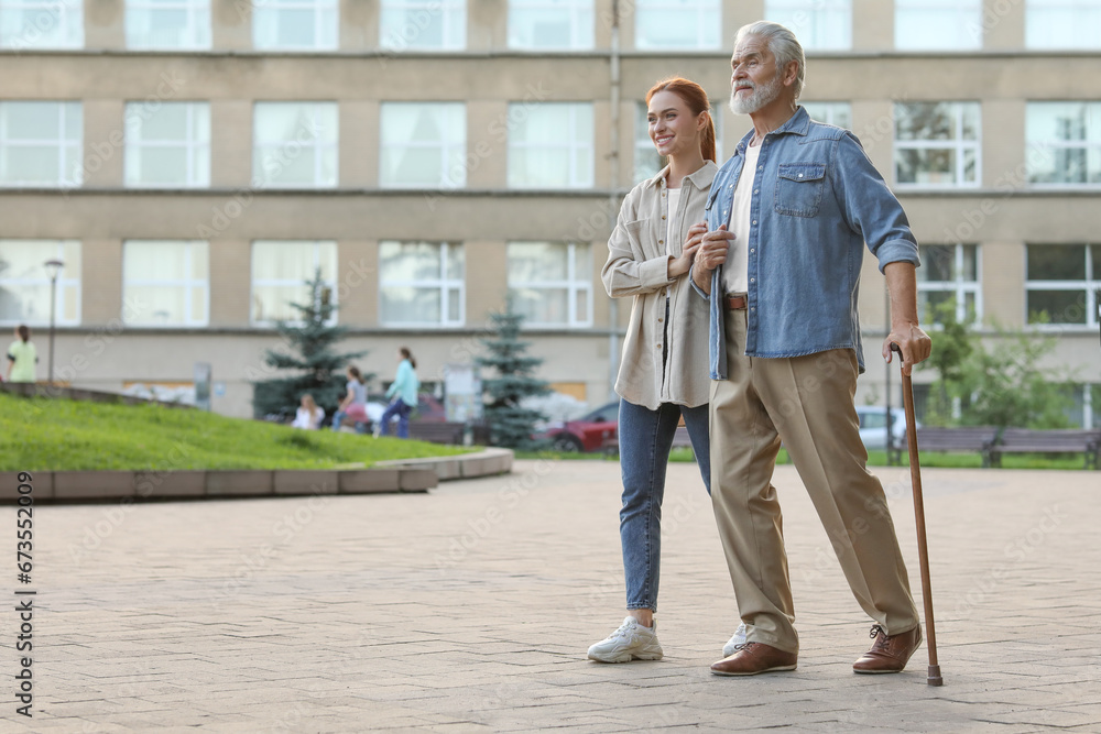 Senior man with walking cane and young woman outdoors. Space for text