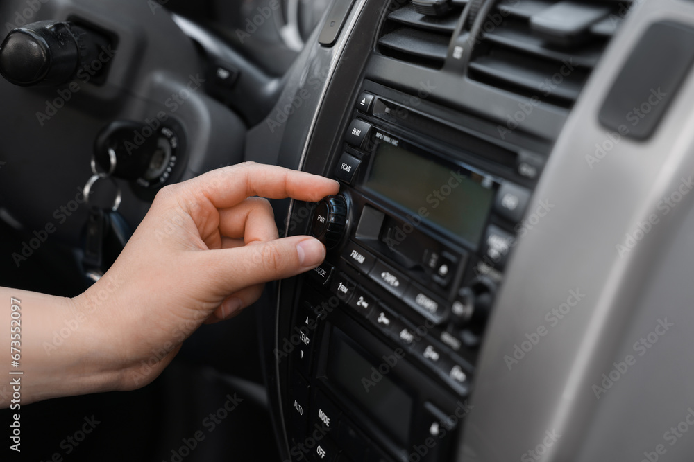 Listening to radio while driving. Woman turning volume button on vehicle audio in car, closeup