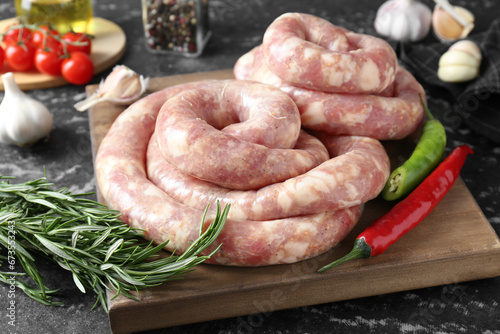 Raw homemade sausage, rosemary, chili peppers and other products on grey textured table, closeup