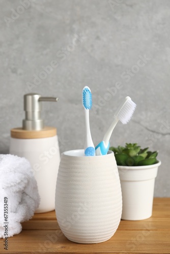 Plastic toothbrushes in holder, towel, potted plant and cosmetic product on wooden table