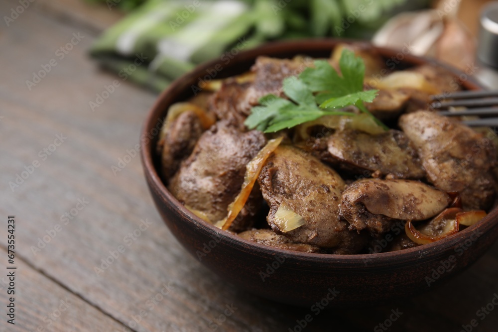 Tasty fried chicken liver with onion and parsley in bowl on wooden table, closeup Tasty fried chicken liver with onion and parsley in bowl on wooden table, closeup