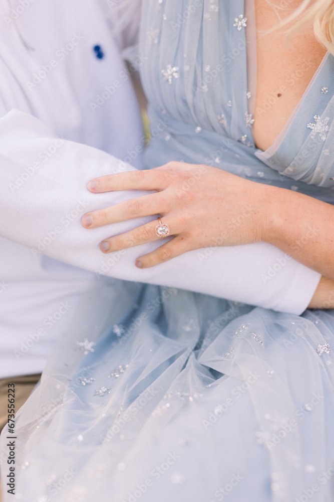 An engaged couple embraces, her hands showing off her engagement ring touches his arm. He wears a white long sleeved t-shirt. An engaged couple embraces, her hands showing off her engagement ring touches his arm. He wears a white long sleeved t-shirt.