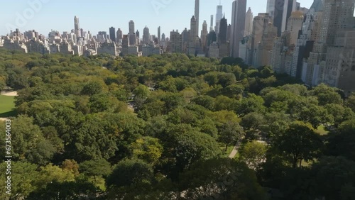 Flying over a building, revealing the sunny Central park of New York - Aerial view