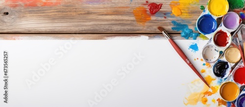Close up flat lay of a watercolor palette paintbrushes and paper on a wooden background The scene has a spring like background with plenty of space for copying