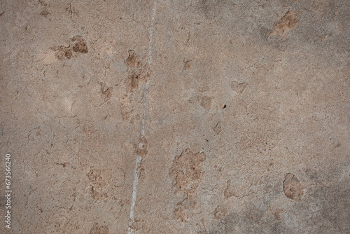 Detail of a deteriorating concrete floor with cracks and pock marks. The concrete has a brown-beige color with hints of grey. photo