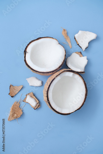 The fresh coconut is divided into two halves and coconut pieces of different sizes are displayed on a blue background. Scene used for many purposes.