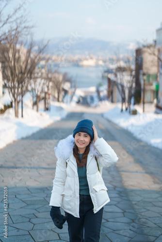 Woman tourist Visiting in Hakodate, Traveler in Sweater sightseeing Hachiman Zaka Slope with Snow in winter. landmark and popular for attractions in Hokkaido, Japan. Travel and Vacation concept