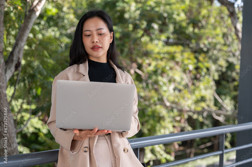 A busy, professional Asian businesswoman is working on her laptop outdoors on the skywalk. A busy, professional Asian businesswoman is working on her laptop outdoors on the skywalk.