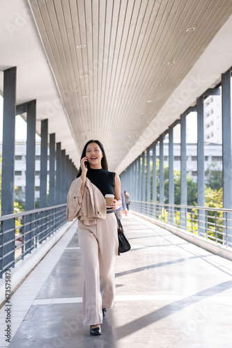 A busy and confident Asian businesswoman is talking on the phone while walking on a skywalk.