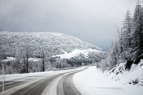 Photo of winter road during the snowfall in Magadan, Russia. Snow showers on trees and hills. Fog and haze, low visibility due to snowstorm. Extreme weather conditions. Car approaching in the distance