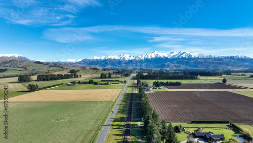 Aerial farming grazing and crop fields in rural  countryside with a backdrop of the snow capped Mountain range under clear skies