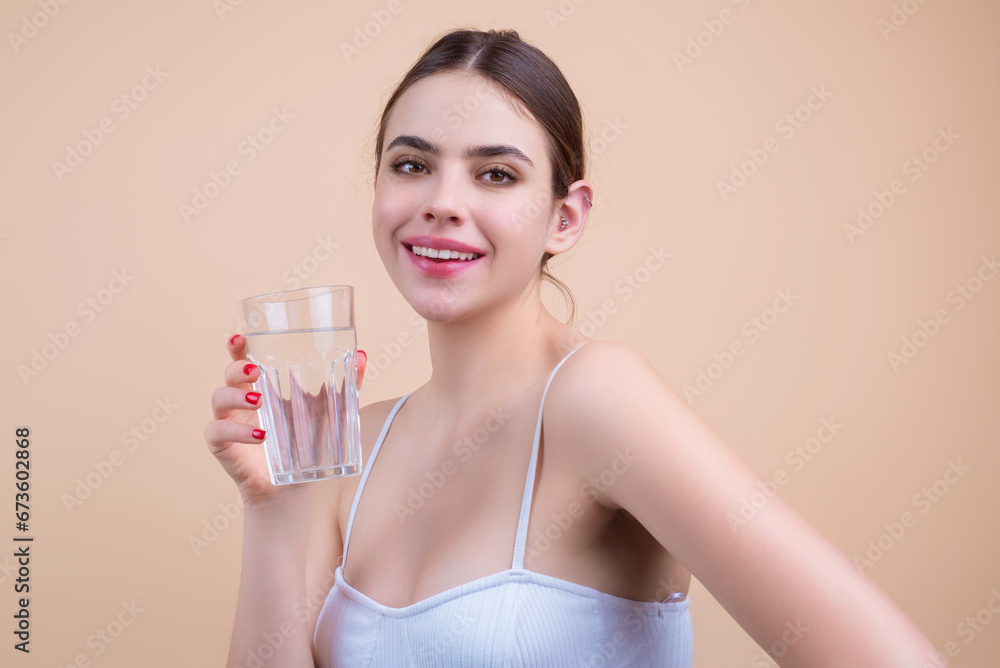 Woman drinking a fresh glass of water, isolated on studio background. Thirsty woman holding glass drinks water. Dehydration, hydration, water balance. Portrait of girl drinking pure water from glass. Woman drinking a fresh glass of water, isolated on studio background. Thirsty woman holding glass drinks water. Dehydration, hydration, water balance. Portrait of girl drinking pure water from glass.