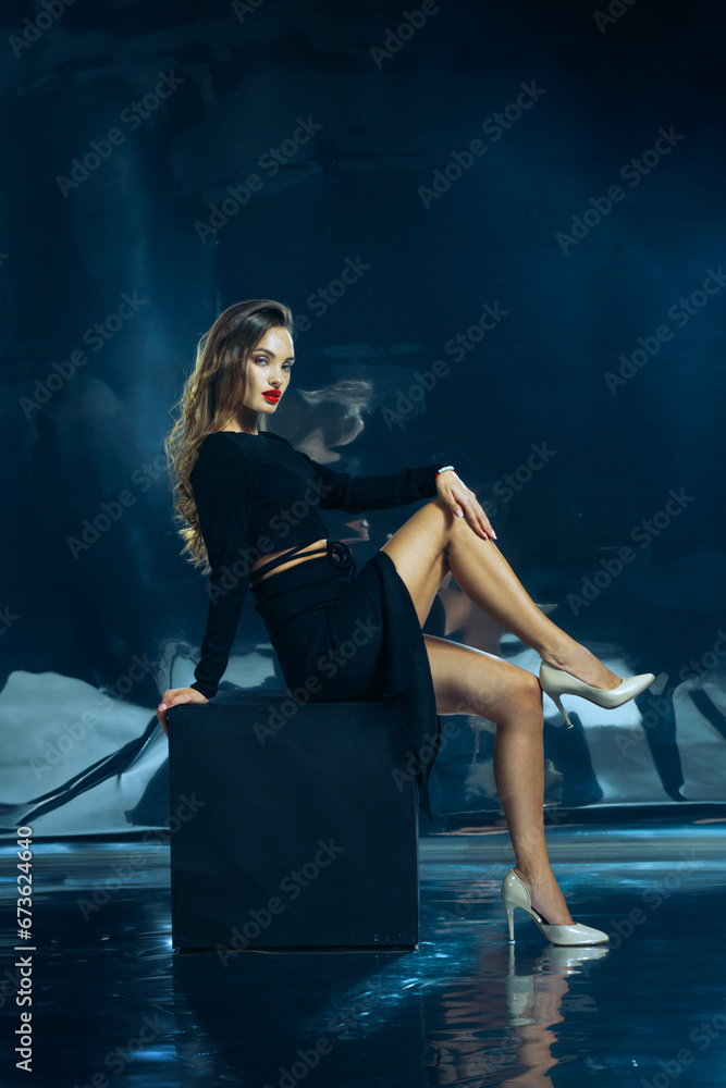 Sexy lady in black dress posing in studio on dark foil background