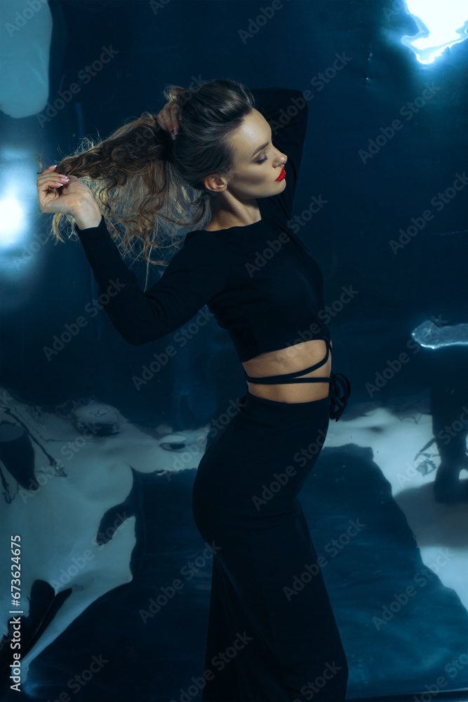 Sexy lady in black dress posing in studio on dark foil background