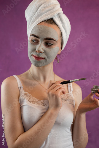 Woman applying with brush green clay mud mask to her face isolated violet photo