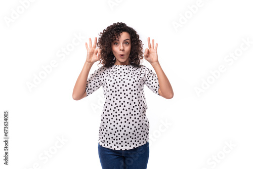 young surprised well-groomed brunette curly woman dressed in a polka dot print blouse