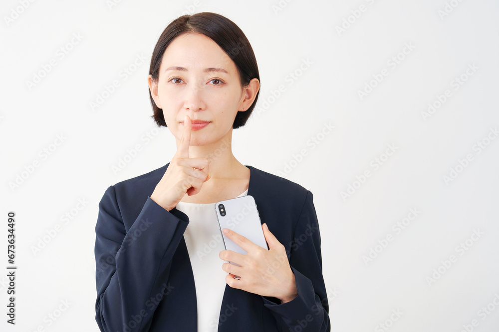 スマートフォンを持って秘密のポーズをする中年のビジネスウーマン　白背景