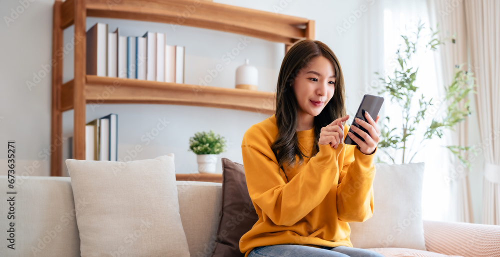 Happy young asian woman relax on comfortable couch at home texting messaging on smartphone, smiling girl use cellphone chatting, browse wireless internet on gadget, shopping online from home Happy young asian woman relax on comfortable couch at home texting messaging on smartphone, smiling girl use cellphone chatting, browse wireless internet on gadget, shopping online from home