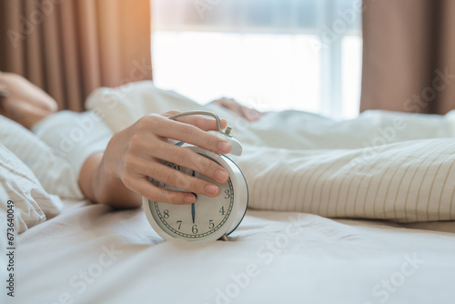 alarm clock and asian woman hand stop time in bed while sleeping, young adult female wake up late in the early morning. Relaxing , sleepy, daily routine and have a nice day concepts photo