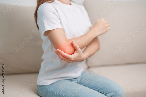 Woman having elbow ache during sitting on couch at home, muscle pain due to lateral epicondylitis or tennis elbow. injury, Health and medical concept photo