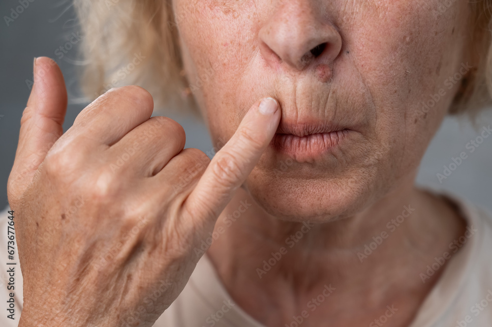 Naklejka premium Unhappy elderly woman pointing at wrinkles around her lips.