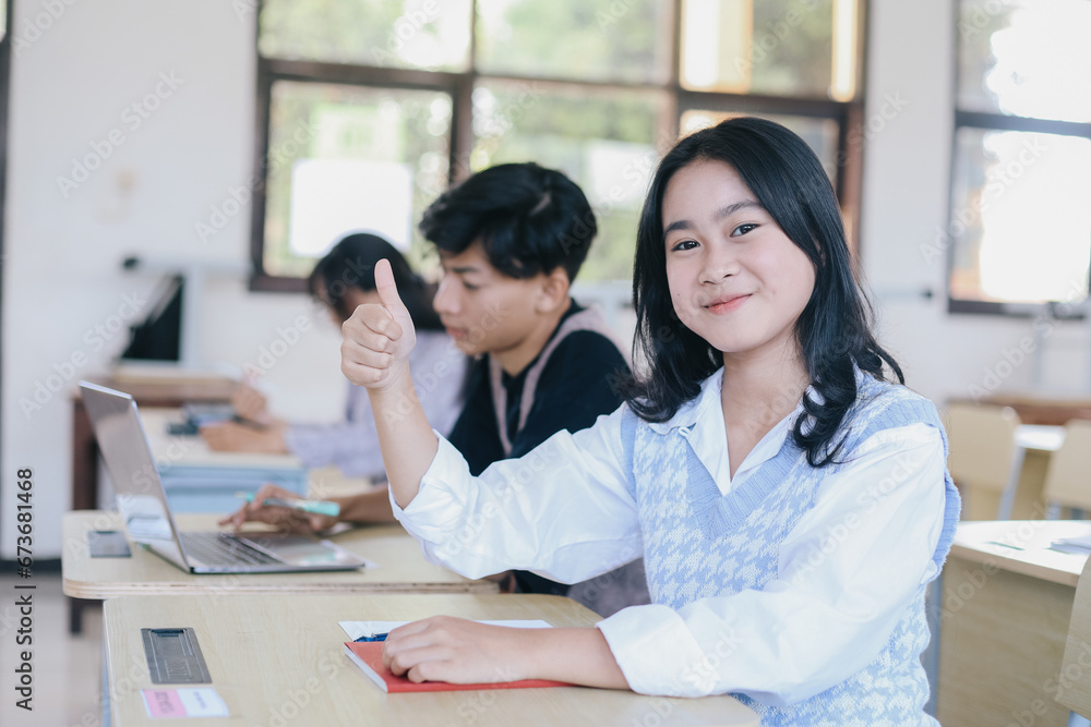 Portrait of smiling asian female student sitting while giving thumb up at desk in classroom at university Portrait of smiling asian female student sitting while giving thumb up at desk in classroom at university