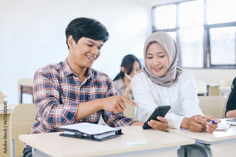Happy college students looking at mobile phone together in classroom Happy college students looking at mobile phone together in classroom