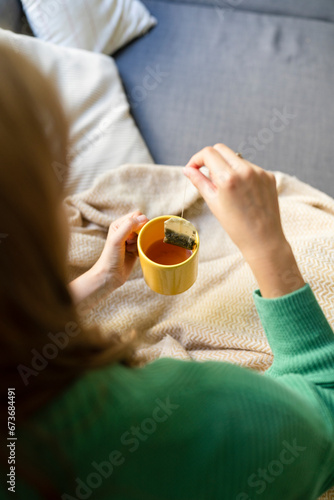 Woman dipping teabag in mug on sofa at home