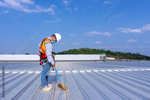 Worker wearing full safety body harness holding a broom in hand  working on roof top for cleaning metal roof sheet photo