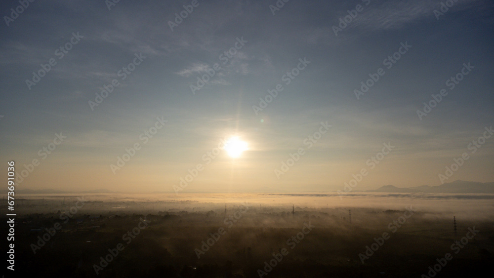 Aerial view of High voltage grid tower with wire cable at tree forest with fog in early morning. Colorful landscape with woods in fog, sunbeams, sky, forest in winter morning.