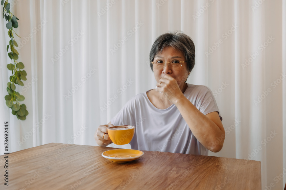 Asian old woman wear eye glasses holding cup and drinking coffee tea, alone at home cafe, Happy smiling, relaxing time, good health care senior insurance lifestyle concept, sitting over white curtain. Asian old woman wear eye glasses holding cup and drinking coffee tea, alone at home cafe, Happy smiling, relaxing time, good health care senior insurance lifestyle concept, sitting over white curtain.