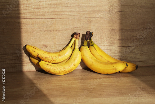 Bananas on wooden kitchen counter. Ripe bananas isolated on table. Sunlight fruits. Quick healthy morning snack. Yellow fruits with brown stains.