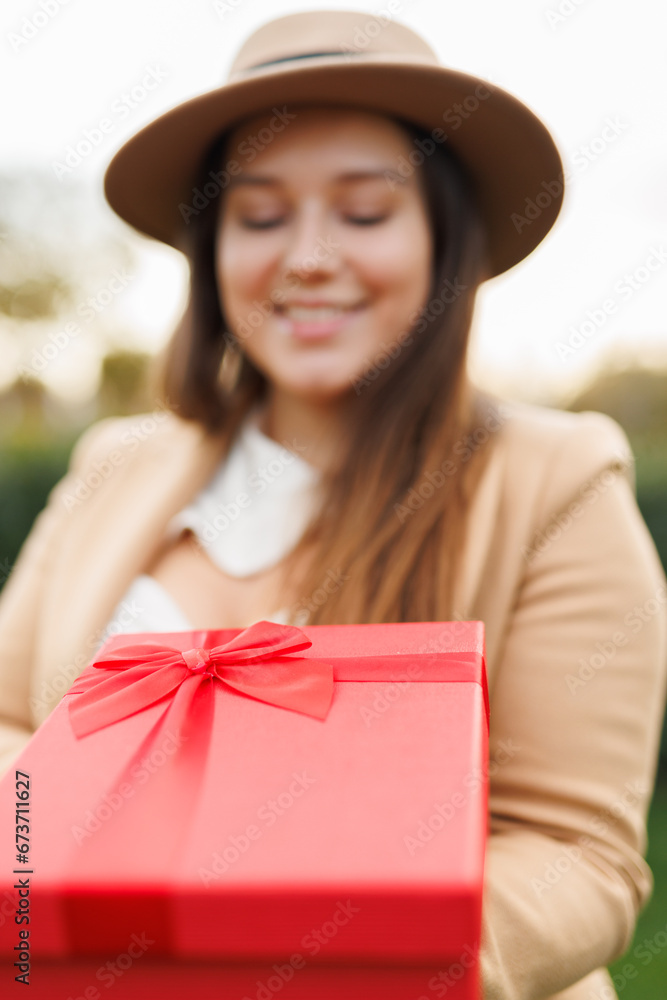 Portrait of charming lady in beige classic coat holding present box in autumn park at sunset. Vertical frame. Portrait of charming lady in beige classic coat holding present box in autumn park at sunset. Vertical frame.