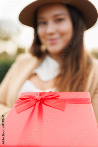 Portrait of charming lady in beige classic coat holding present box in autumn park at sunset. Vertical frame.