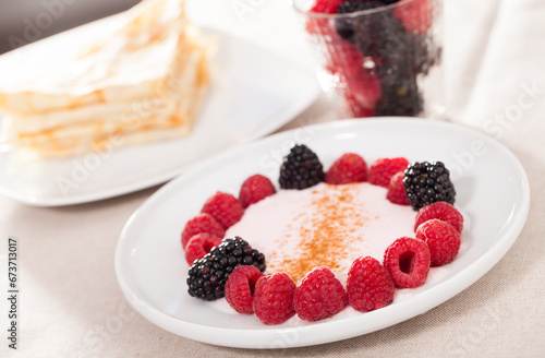 Breakfast of raspberries and blackberries with yogurt and pancakes on table