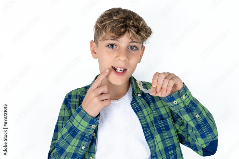 caucasian kid boy wearing plaid shirt holding an invisible aligner and pointing to her perfect straight teeth. Dental healthcare and confidence concept. caucasian kid boy wearing plaid shirt holding an invisible aligner and pointing to her perfect straight teeth. Dental healthcare and confidence concept.